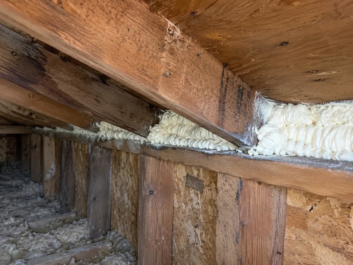 Illustration of close attic roof-wall joint with cream foam and aged dry wood, realistic uneven texture