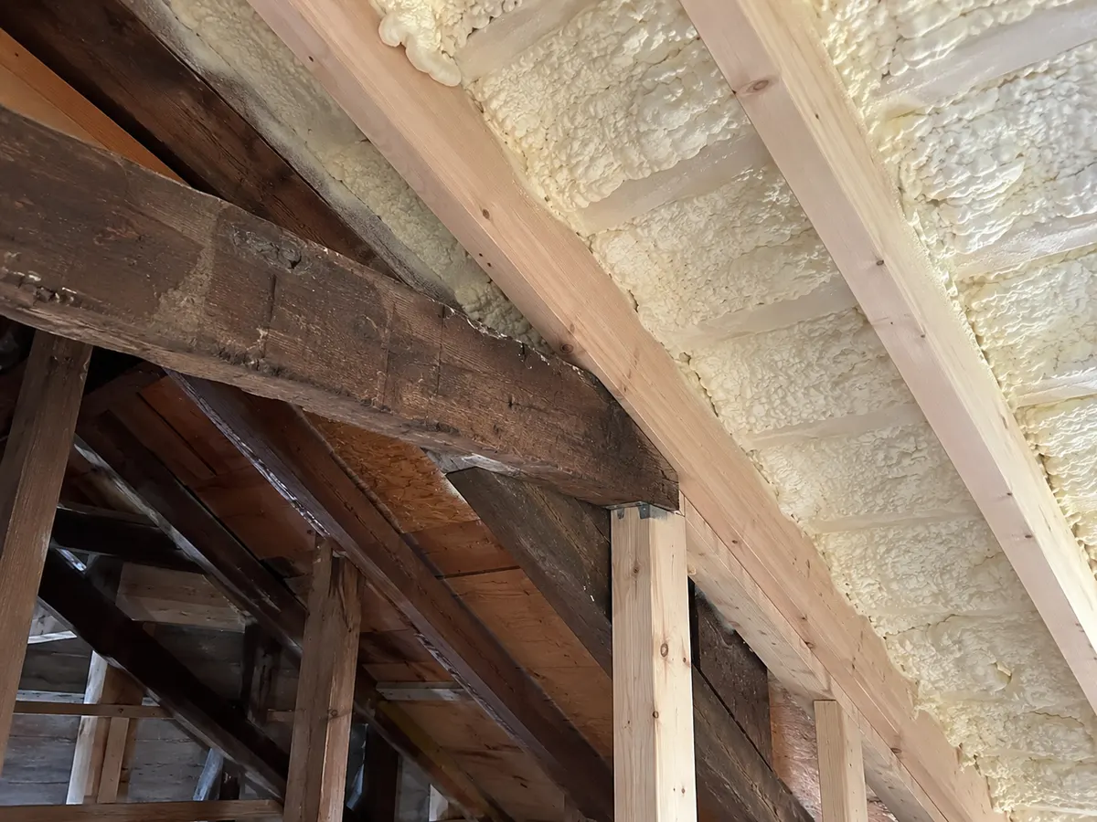 Illustration of close roof intersection where old and new timber framing meet, pale foam between rafters
