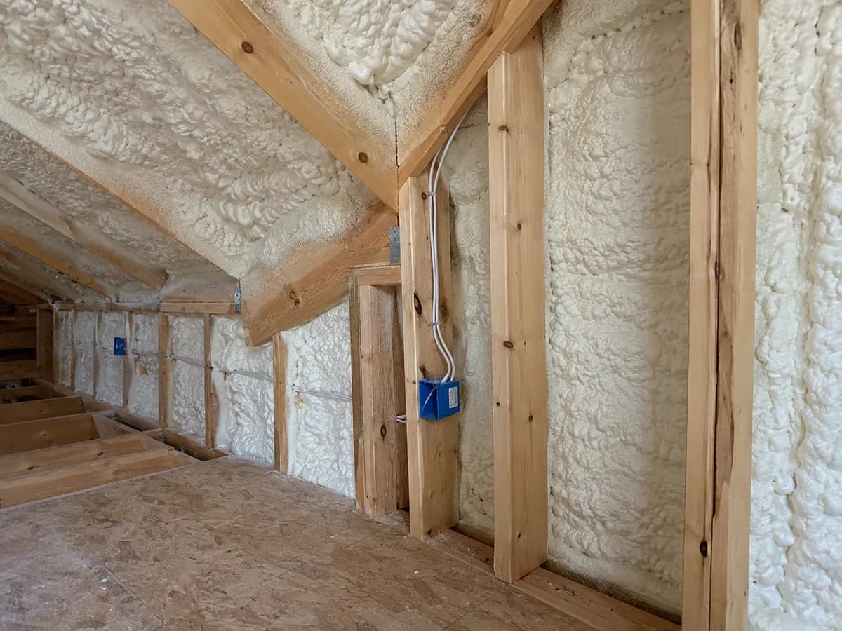 Illustration of framed attic roof-wall corner with white insulation and masked electrical rough-ins