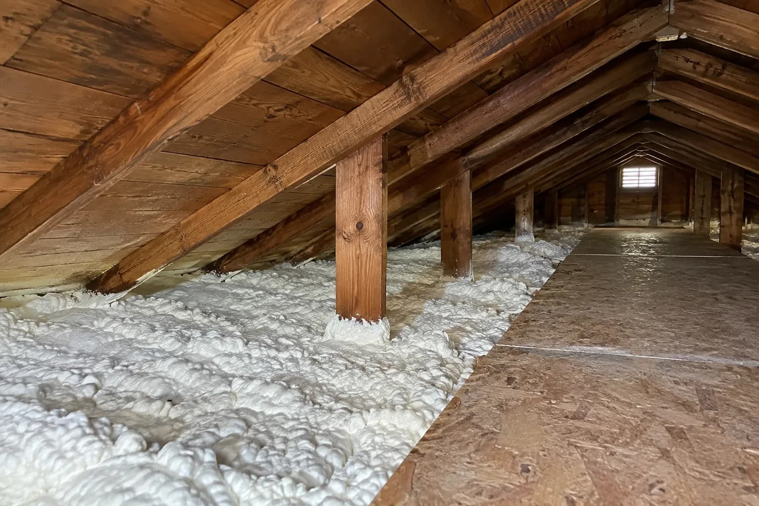 Illustration of low residential attic with white foam beneath aged rafters, exposed timber ties and a clean accessible walkway
