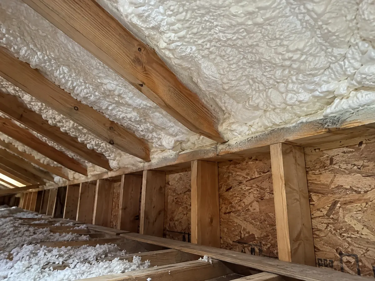 Illustration of close attic eave area showing white foam between rafters and a roof-wall transition