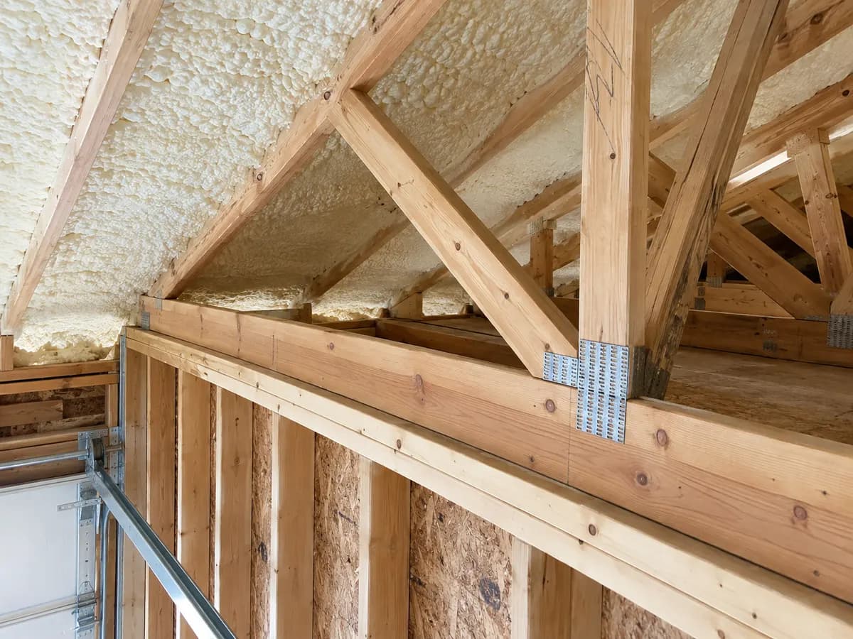 Illustration of attic framing junction over a garage wall, cream foam and intact timber with clear service space