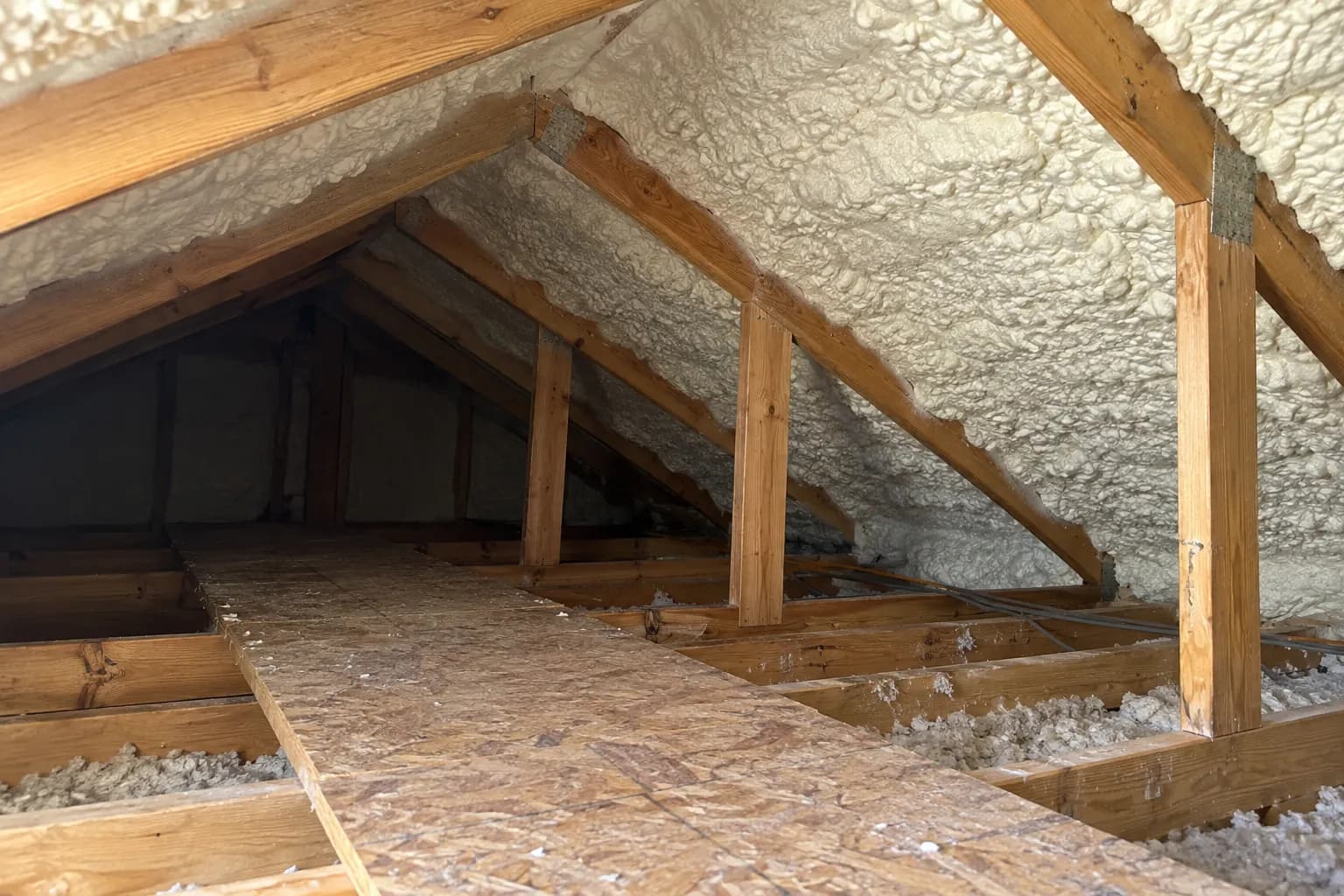 Illustration of low residential attic roof with white open-cell foam and existing plywood access walkway, soft afternoon light