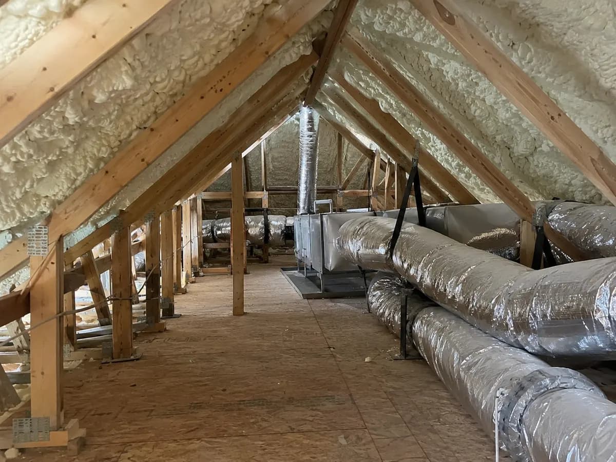 Illustration of attic mechanical service zone kept clear beneath insulated roof slopes, ducts protected and no workers