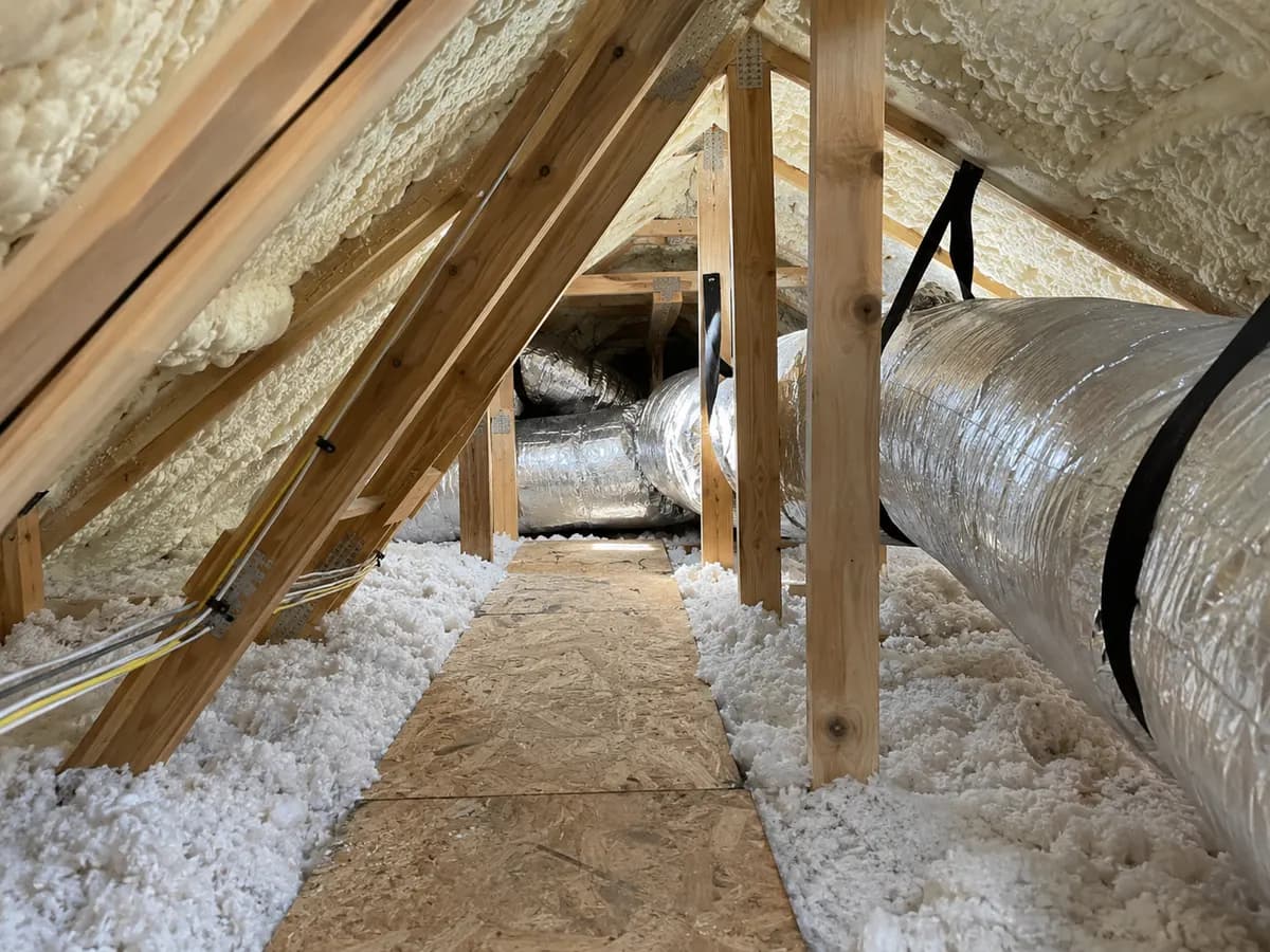 Illustration of attic mechanical access path under insulated rafters, protected wiring and realistic duct scale