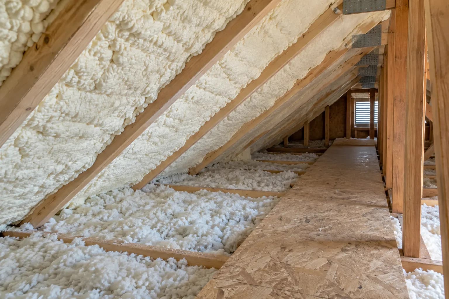 Illustration of modest house attic with pale foam following a low roofline and a plywood service walkway, natural side light